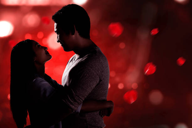 Beautiful young couple standing, looking at each other and hugging among Christmas lights in the city
