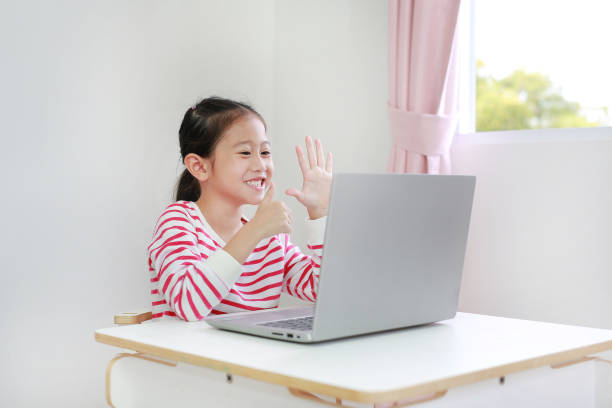 istock Little asian schoolgirl study online learning class by video call on laptop computer with teacher during new normal Covid-19 coronavirus at home. 1299911269