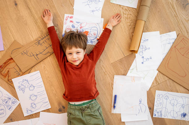 istock Kid lying down on the floor surrounded by his drawings 1299914360
