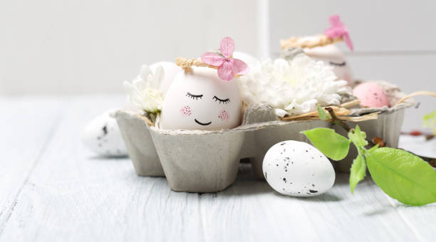 istock Easter holiday concept with cute handmade white eggs, tree branches, quail feathers and spring flowers on white wooden background. 1299914643