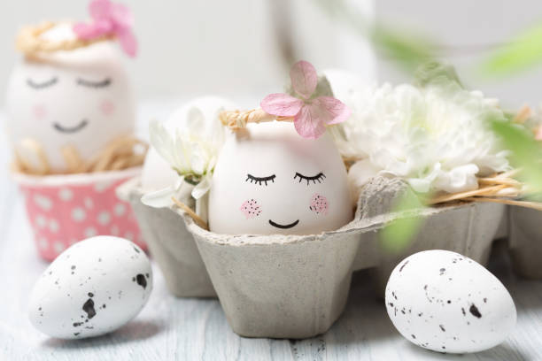istock Easter holiday concept with cute handmade white eggs, tree branches, quail feathers and spring flowers on white wooden background. 1299914660