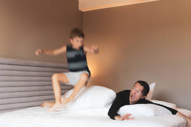 istock Boy in blurred motion jumping while plying with father in bedroom. 1299918046