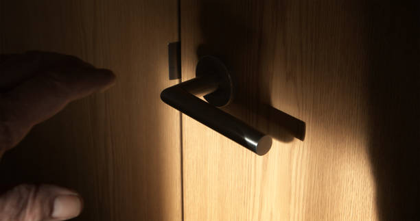 Shadowy man's hand about to open a door handle.