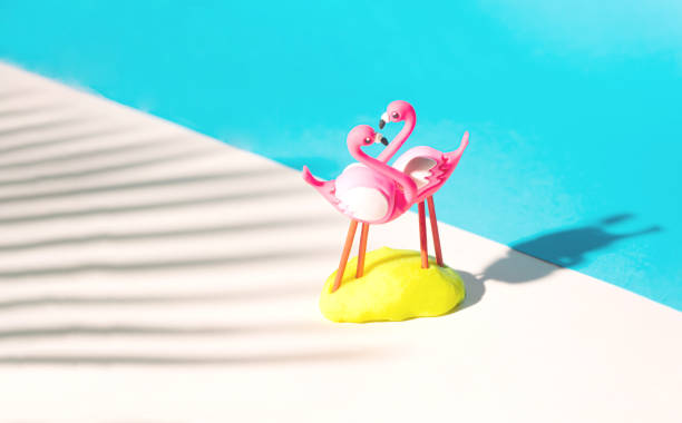 istock Two flamingos toys with shadow from palm leaf with copy space. 45 degree angle level shoot with beige and pastel blue background. 1299920608