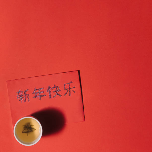 une tasse chinoise de thé avec le thé vert sur la surface rouge. enveloppe chanceuse rouge avec le salut de « bonne année » dans les caractères cantonais. nouvel an lunaire 2021. - symbol china ideas gold leaf photos et images de collection