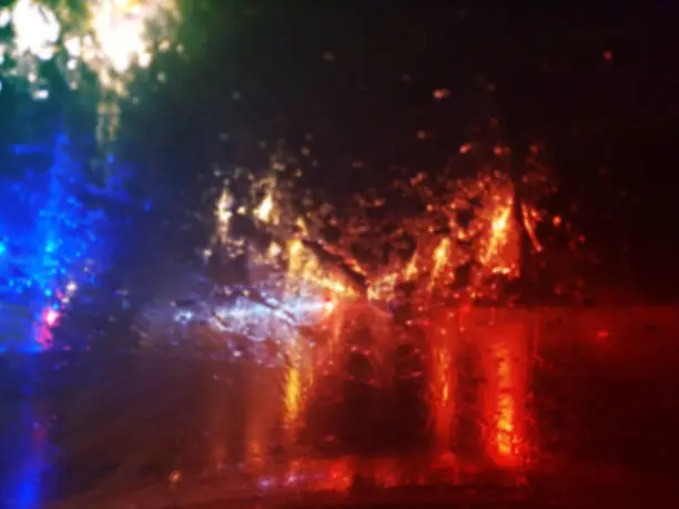 Photo of view from car on raindrops on window and road with police lights and silhouettes of cars driving behind him in rainy evening