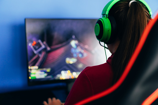 A young girl playing a computer game on professional armchair against monitor in green headphones, live stream, esports.