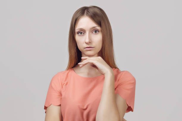 istock Pensive blond girl with thoughtful expression, keeps hand on chin, plans something or makes choice 1299923613