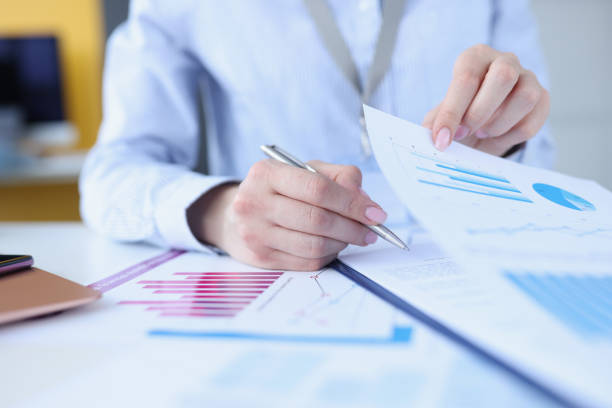 istock Woman signing document with graphs with ballpoint pen closeup 1299924020