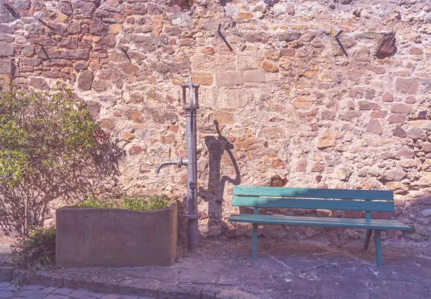 an old water pump in front of a stone wall with a green bench
