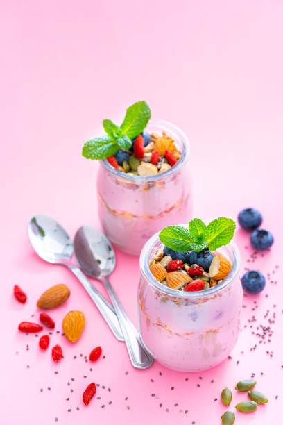 Healthy food backgrounds: high angle view of two yogurt glass containers with blueberries, almonds, pumpkin seeds, goji berries and chia seeds shot on pastel pink background. Goji berries, blueberries, almonds, pumpkin seeds and chia seeds are around the yogurt containers. High resolution 42Mp studio digital capture taken with Sony A7rII and Sony FE 90mm f2.8 macro G OSS lens
