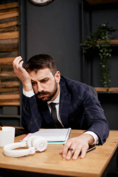 istock Tired man sitting at office desk drinking coffee. 1299929312