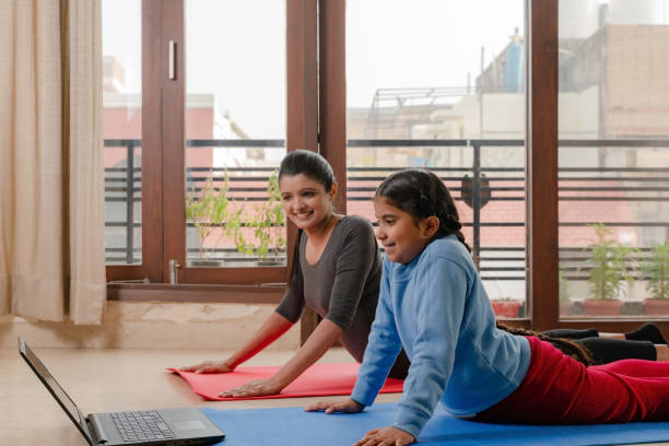 mutter und kleines mädchen beim yoga zu hause - yoga good posture women little girls stock-fotos und bilder