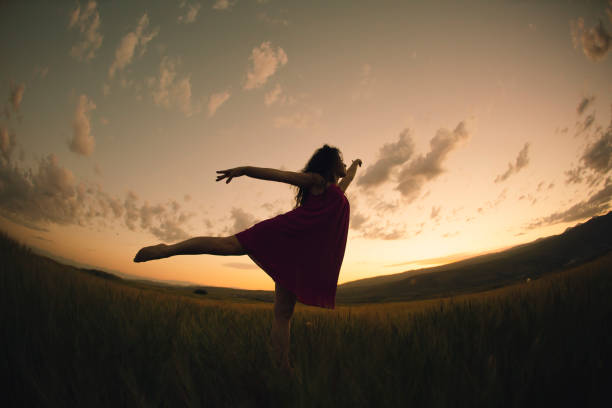 Young talented dancer girl raises her leg in the field of wild flowers during the gorgeous sunset