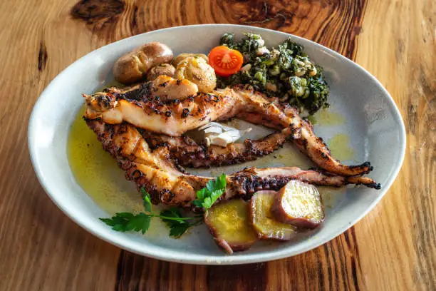 Photo of Popular portuguese grilled octopus plate with sweet potatoes and some green vegetables.