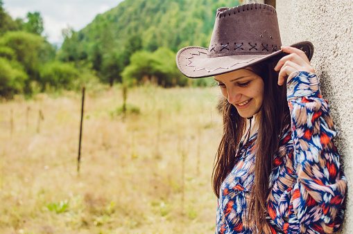 Portrait of a young cowgirl, wearing cowboy hat, posing against summer nature.
