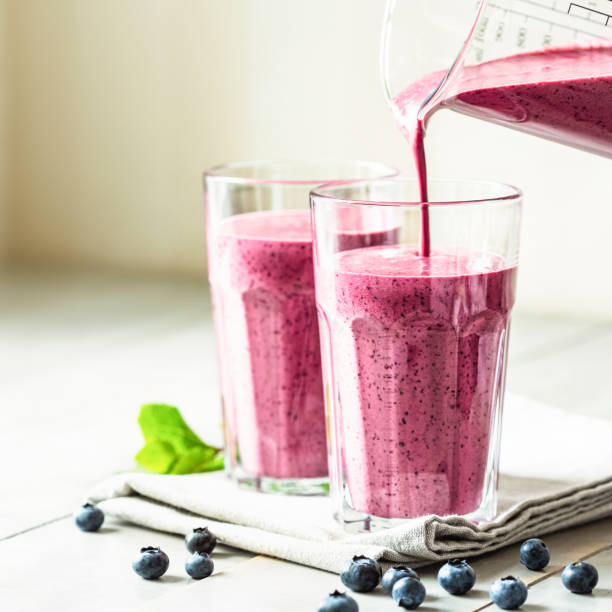 Two glasses of blueberry smoothie. Two glasses of blueberry smoothie with mint garnish and straw on the table. Berry shake is poured into a glass. straw photos stock pictures, royalty-free photos & images