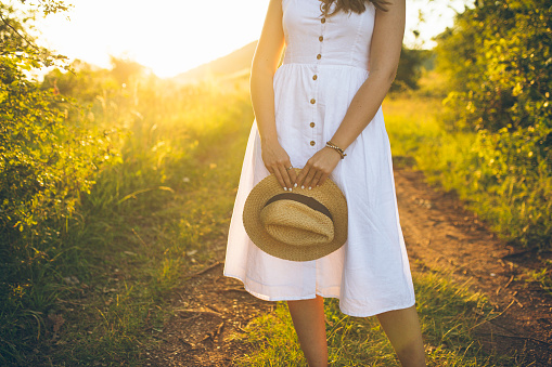 Woman in white dress holding a straw hat, relaxing in nature