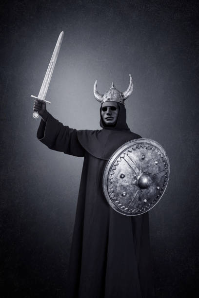 istock Scary figure with horned helmet, sword and round shield in the dark 1299941935