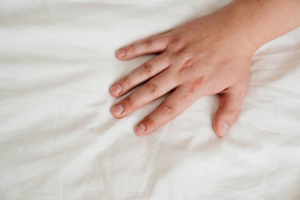 istock man's hand on a white bed sheet. skin care products. 1299943718