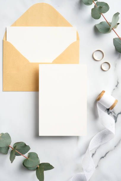 istock Wedding invitation card, rings, envelope, eucalyptus branches on marble table. Flat lay, top view. 1299944246