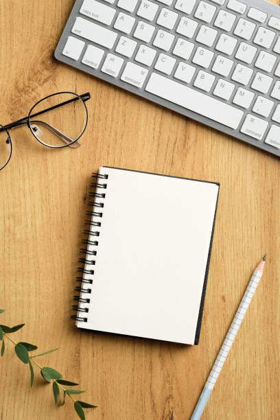 istock Top view blank notebook with keyboard, glasses and eucalyptus leaves on wooden table. Modern feminine workspace concept. 1299944265