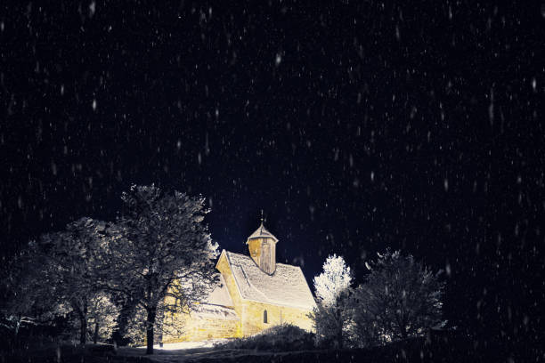 Old medieval church lit up on a cold winters night during a blizzard with visible snow.
