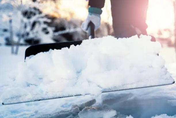 Photo of Close up of a person clearing snow from the sidewalk with a snow shovel.