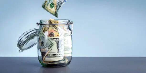 Photo of Money in cash box over gray background with copy space. Donations charity concept. Dollars with glass jar for money saving financial.