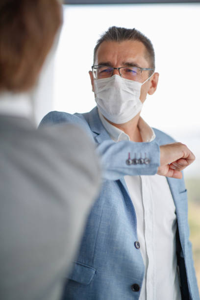 istock Businessman wearing protective face mask and greeting partner with elbow bump 1299948021