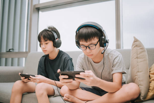 asian chinese brother playing multiplayer online gaming with headset in living room using smart phone connection asian chinese brother playing multiplayer online gaming with headset in living room using smart phone connection asian child playing video games stock pictures, royalty-free photos & images