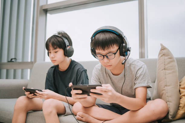 asian chinese brother playing multiplayer online gaming with headset in living room using smart phone connection asian chinese brother playing multiplayer online gaming with headset in living room using smart phone connection asian teen phone stock pictures, royalty-free photos & images