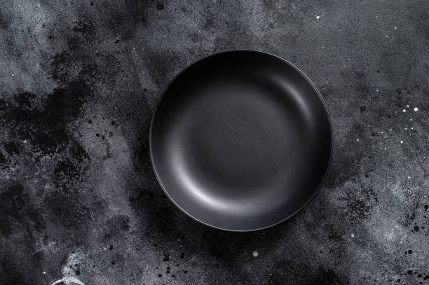 istock Black plate on textured black background.  Top view. Copy space 1299949476