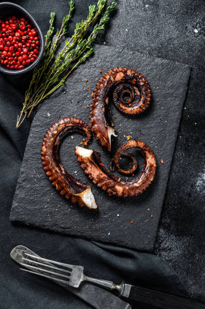 istock Fried octopus tentacles with thyme and pink pepper. Fresh seafood. Black background. Top view 1299954453