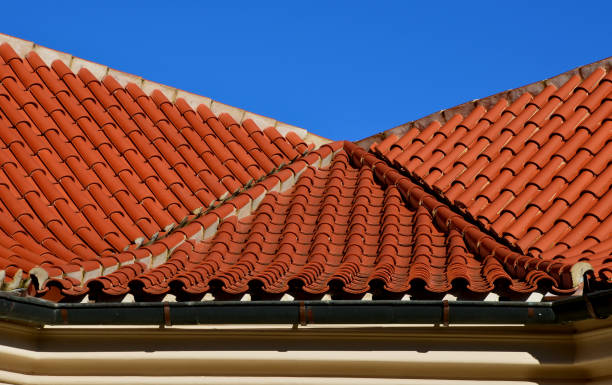 la vaguada de dos techos doblado en un giro con azulejos plegados italianos y una alcantarilla de metal. se puede ver la cresta del techo con tejas de hormigón, cielo soleado, azul - roof tile roof textured red fotografías e imágenes de stock