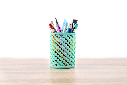 Green plastic basket  with colorful pen and Cutter or stationery put on wooden table  isolated on white background