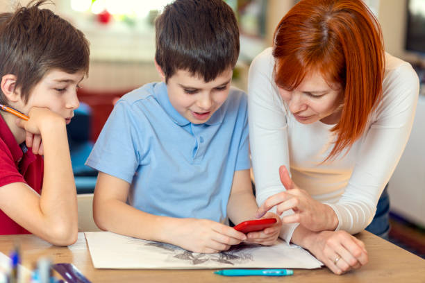 istock Two smiling boys using smartphone with their mother at home 1299957378