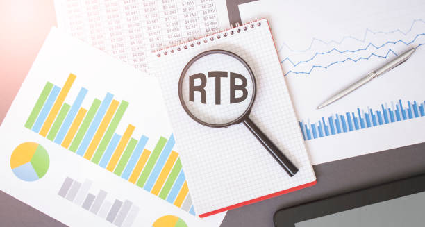 istock Magnifying glass on RTB text on notepad, dice, spectacles, pen, laptop calculator on wooden table - business, banking, finance and investment concept 1299961589