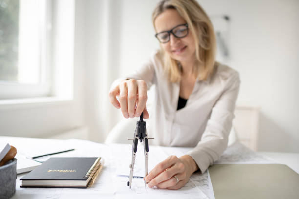 istock beautiful, young and blond female architect is drawing something with a compass in a plan 1299961687