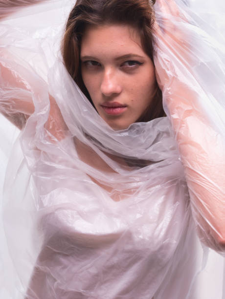 istock conceptual portrait, one young beautiful woman wraped in plastic sheet. Shot in studio, white background. 1299963064