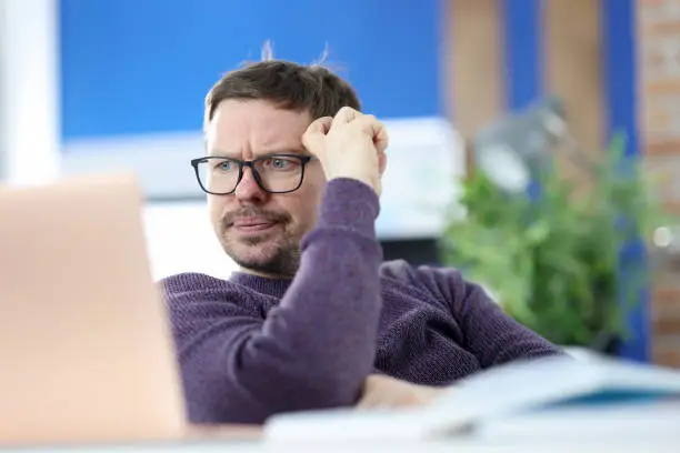 Photo of Disgruntled man with glasses looking at laptop screen