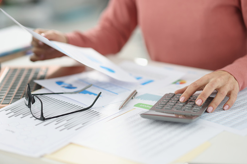 Mujer de negocios contando con calculadora y sosteniendo documentos en las manos de cerca photo