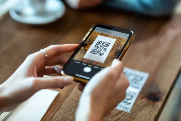 Photo of Young woman hands using the smart phone to scan the qr code to select food menu in the restaurant.