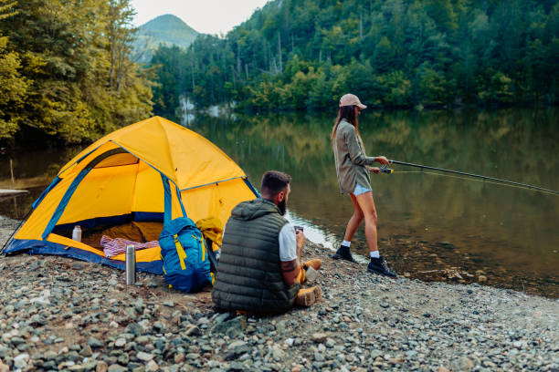 We always make time for fishing Young woman out fishing by a river while his boyfriend making company freshwater fishing stock pictures, royalty-free photos & images