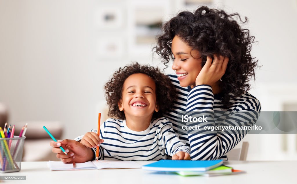 Excited ethnic mother and son doing homework Cheerful ethnic woman laughing while helping happy boy to do homework assignment in cozy room at home Mother Stock Photo