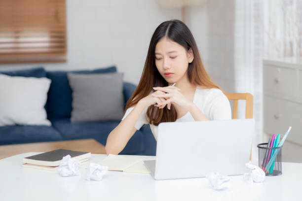 istock Young asian woman working with laptop computer think idea project and paper crumpled having problem on table at home, girl using notebook with frustrated and trouble, business and freelance concept. 1299970106