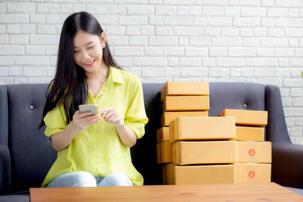 istock Young asian woman is entrepreneur check order from smartphone with customer while purchase online, logistic and delivery, online shopping, female is seller of business SME, merchant looking phone. 1299970415