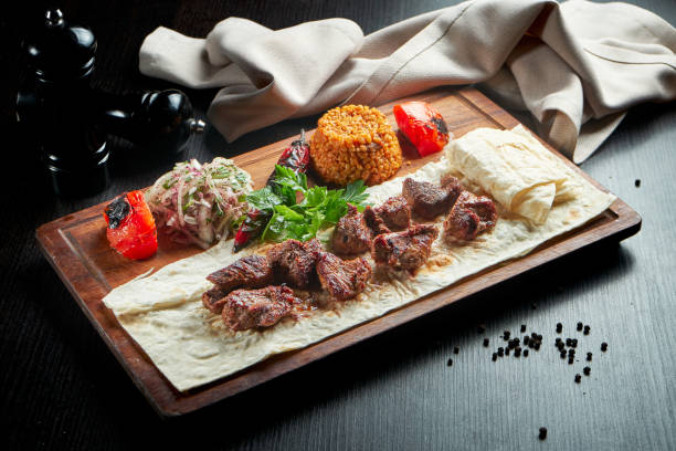 istock Appetizing beef kebab with grilled vegetables, bulgur and pickled onions on a wooden board 1299972058