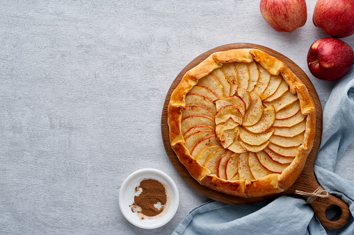 Apple pie, galette with fruits, sweet pastries on gray backdrop, sweet crostata on cutting wooden board, side view, autumn or winter food, copy space, top view