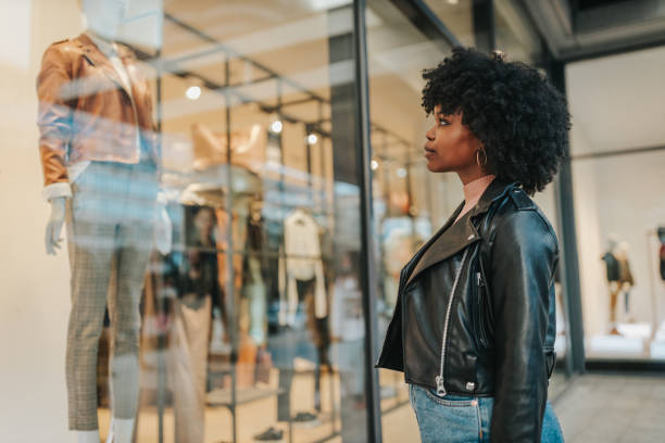 Afro female standing in front of shop window A young woman out shopping in the city. Afro female standing in front of boutique and looking in the shop window window shopping stock pictures, royalty-free photos & images